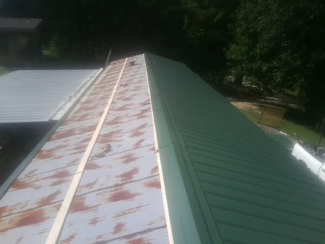 Old rusted panels beside newly installed green metal roofing — Wind Damage Roof Repair by Roofing Brothers in Montross