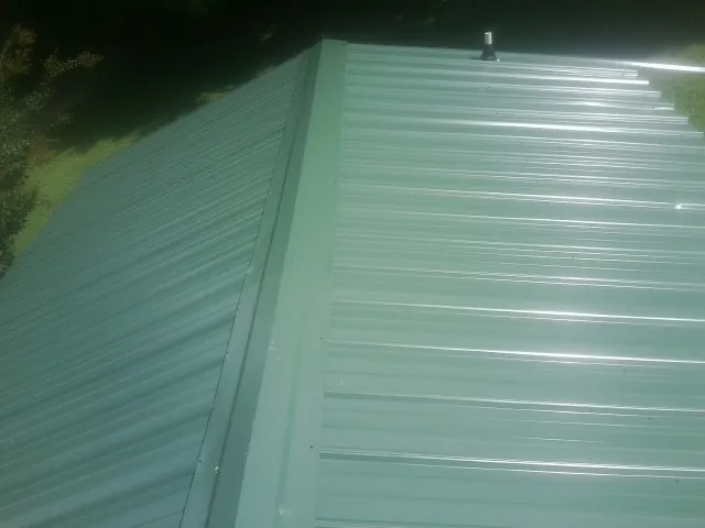 New green metal panels meeting at the ridge of a roof — Flat Roof Repair work by our crew in Montross