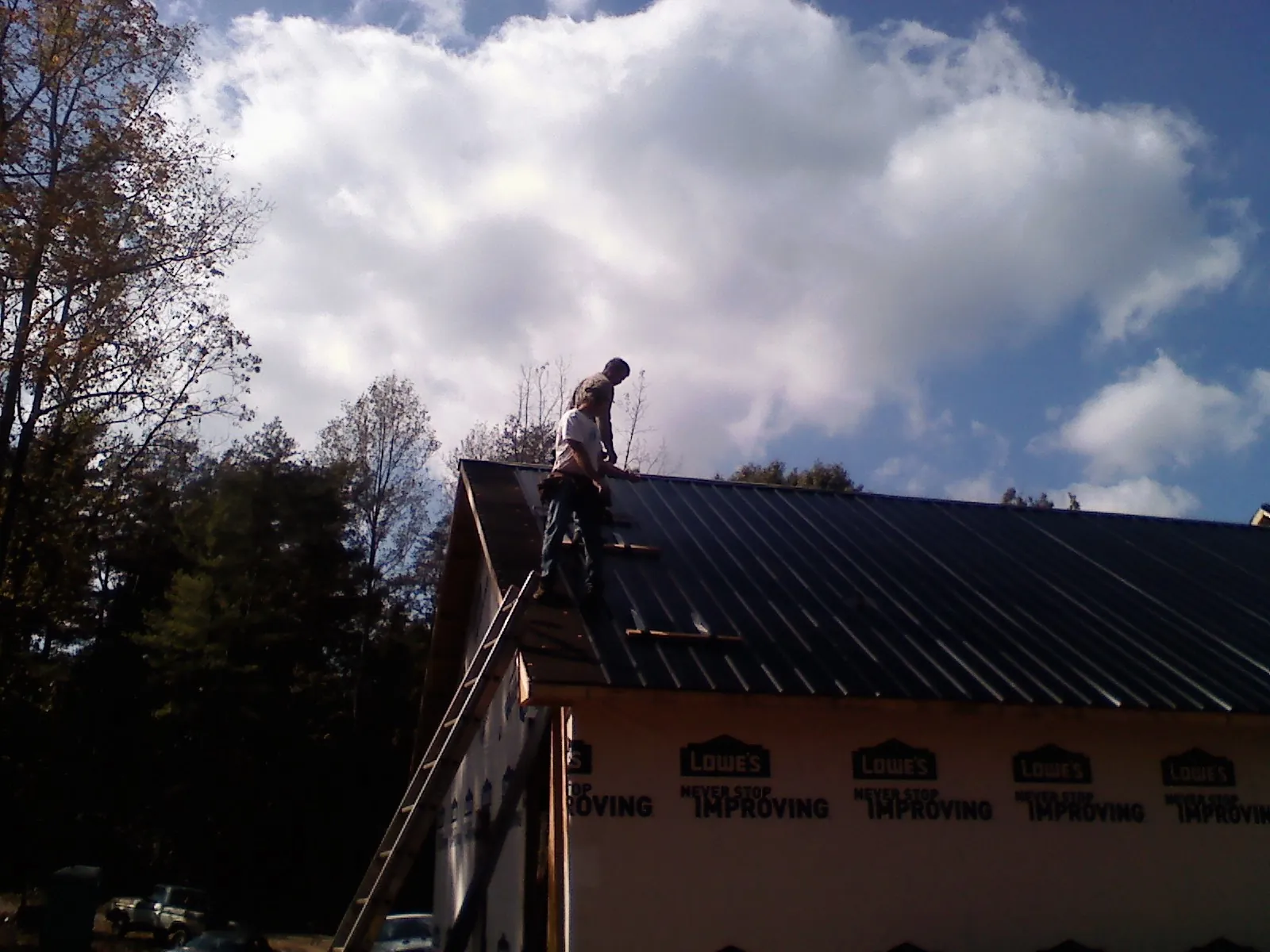 Roofer fastening dark metal panels high against a cloudy sky, from a Roof Inspection job in Montross